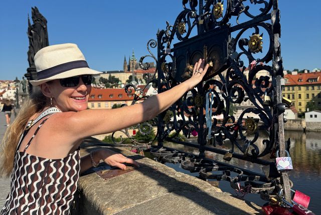 Гостья у решётки Карлова моста, за рекой — Пражский Град